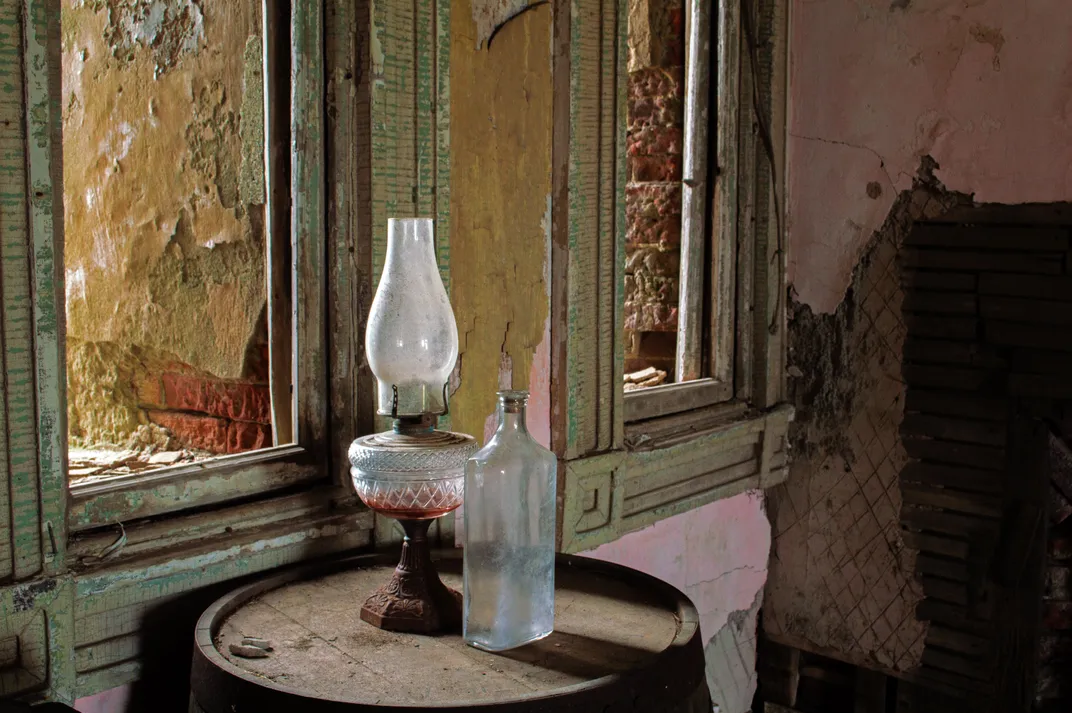 13 - An abandoned bottle and an oil lamp rest on a barrel in a weathered room at Fort Adams.