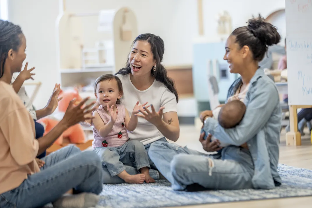 three women and their small children are seated in a circle, some smiling and clapping